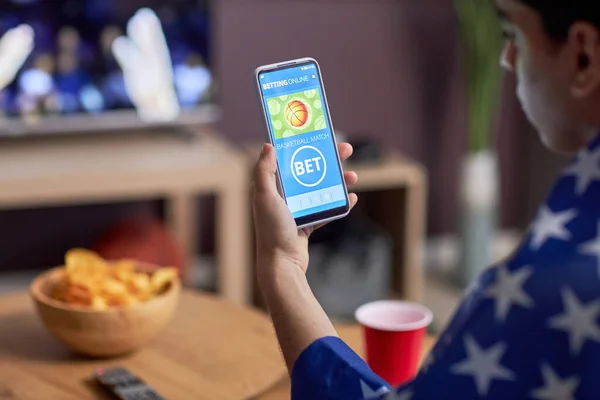 Closeup of basketball fan using sports bets app while watching match at home, copy space