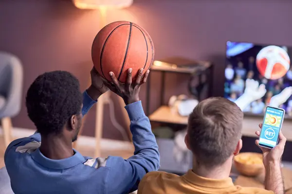 和朋友一起在家里看体育比赛时拿着篮球的黑人年轻人的倒影 — 图库照片