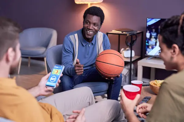 Diverse group of sports fans watching basketball match at home and using online betting app