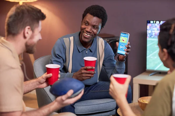 Diverse group of friends watching sports match at home and using online betting app