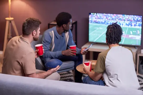 在家里看电视上看美式足球比赛的各色人等的朋友的回顾 — 图库照片