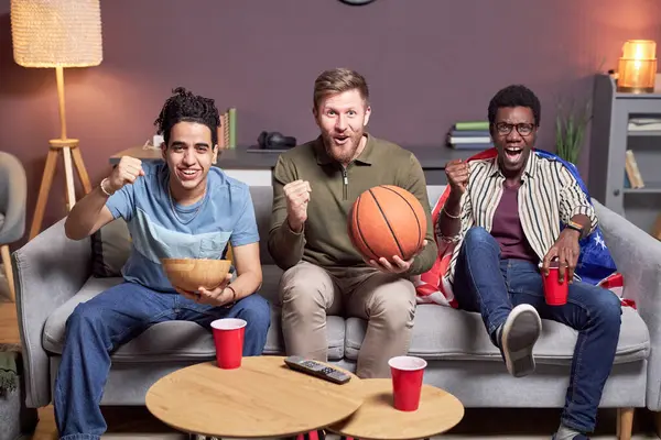 Diverse group of friends watching sports match at home and having fun cheering emotionally