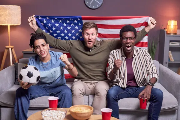 Diverse group of sports fans watching match on TV at home and waving USA flag