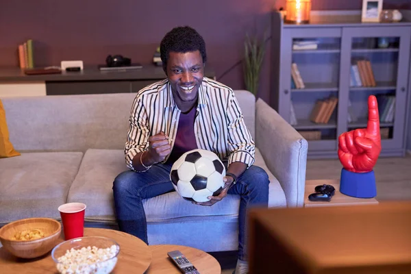在家里看电视上看足球比赛 拿着蓝光球的年轻黑人形象 — 图库照片