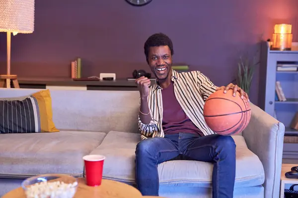 在家里看电视上看篮球赛 拿着蓝光球的黑人年轻人的画像 — 图库照片