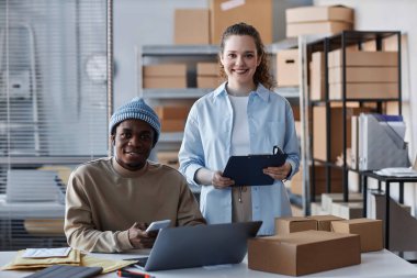 İki mutlu kültürler arası çalışan iş yerinde dizüstü bilgisayarla kameraya bakıyor ve yeni siparişler alıyor.