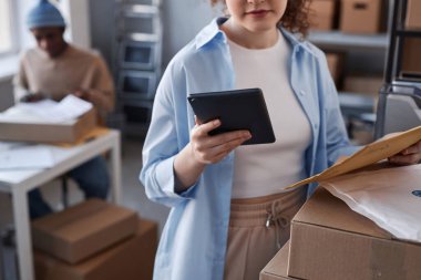 Kadın yöneticinin tablet ile yakın plan çekimleri sipariş sayısını kontrol ederken depolama odasında paketlenmiş kutu ve paketlerin yanında duruyor