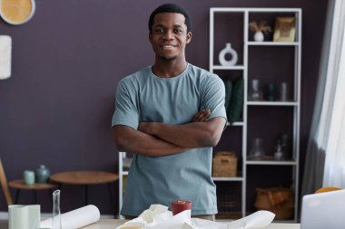 Genç bir erkek mağaza görevlisi ya da zanaat stüdyosunun sahibi elinde ambalaj kağıdı ve satılık bazı el yapımı eşyalar ile iş yerinde bekliyor.