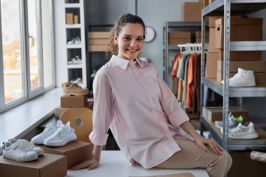 Günlük kıyafetlerle mutlu genç bayan alışveriş meraklısı paketsiz kutularla ve online mağazadan yeni spor ayakkabılarla masada oturuyor.