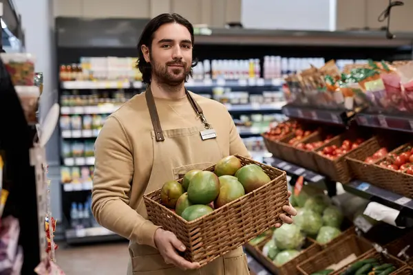 Waist up portrait of young man working in supermarket and carrying box with fresh exotic fruits