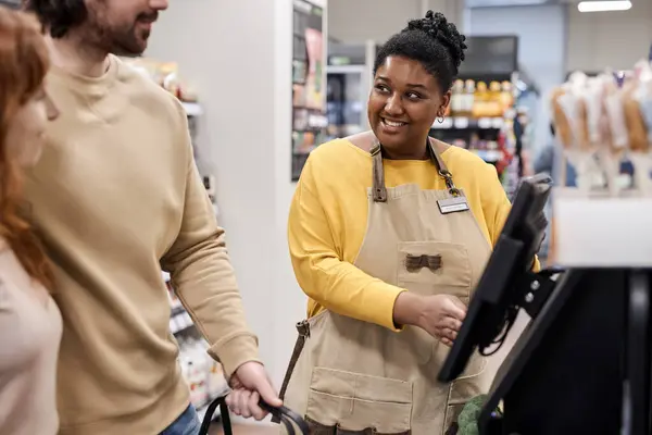 Genç siyahi kadın portresi süpermarkette müşterilere kendi kendini kontrol etme makinesiyle yardım ediyor.