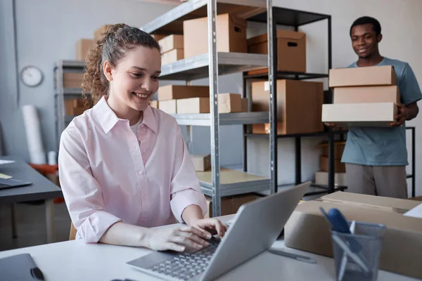 Mutlu genç bir kadın dizüstü bilgisayarda klavyede yazarken Afro-Amerikalı bir adam içinde sipariş edilmiş malların bulunduğu karton kutular taşıyordu.