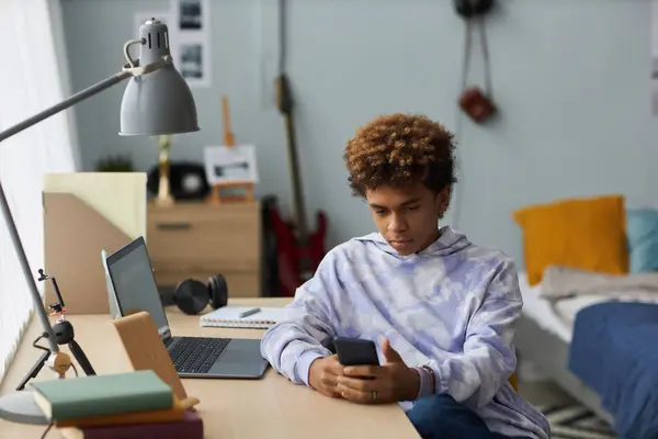 Genç Ciddi Bir Adam Cep Telefonuyla Mesajlaşırken Odasındaki Dizüstü Bilgisayarın — Stok fotoğraf