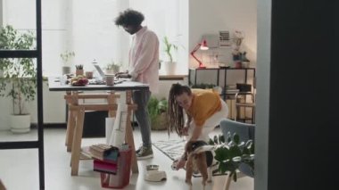 Yaratıcı yerli çalışma alanında birlikte çalışan ırklar arası genç tasarımcıların tam karesi. Çift ırklı adam dizüstü bilgisayarda 3D görüntüleme yaparken beyaz kadın köpekle oynuyor.