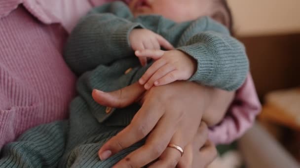 愛と優しさと手でニットロマーを着用する小さな赤ちゃんの男の子を抱いている認識できない母親のクローズアップ — ストック動画