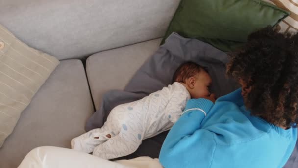 昼間の居心地の良いアパートでソファーの柔らかい毛布に一緒に横たわっている寝ている赤ん坊を介護する母親のトップビュー — ストック動画