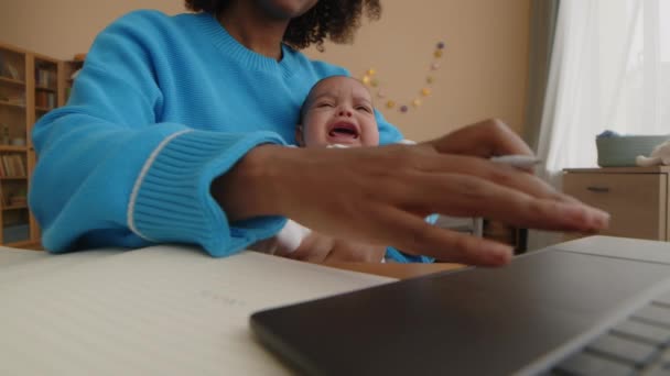 若い黒人女性がコピーブックでノートを取って 彼女の新しい生まれた息子が彼女の腕の中で泣いている間 ノートを使用してクロップされた刺しショット — ストック動画