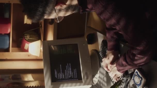 年轻的比尔西亚胡子怪胎坐在窗前书桌前的垂直中低音镜头 在黑暗的房间里关上窗帘 在旧计算机上输入程序代码 — 图库视频影像