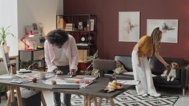 在现代公寓里 一对跨种族的专业室内设计人员一起工作的全景 图纸放在桌子上 猎犬坐在黑色皮革沙发上作为背景 — 图库视频影像