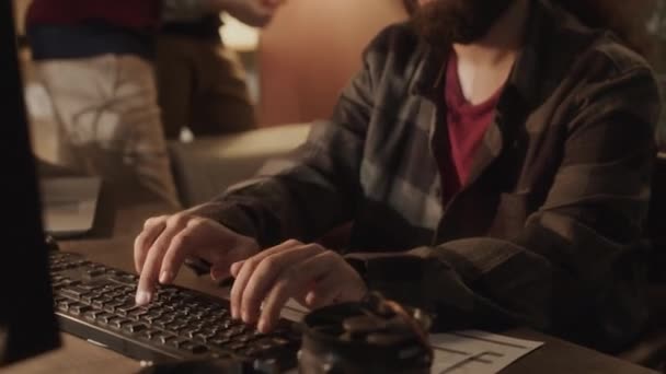 90年代スタイルのオフィスで同僚と仕事をしている間 スクリーンに集中してキーボードに入力する眼鏡に焦点を当てた若い長髪中東の男性コンピュータプログラマー — ストック動画