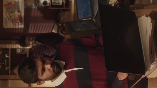 20世纪90年代风格的车库 年轻的Biracial男性程序员穿着条纹复古长袖马球衫 在笔记本电脑上输入代码 与同事们一起工作时的垂直中景照片 — 图库视频影像