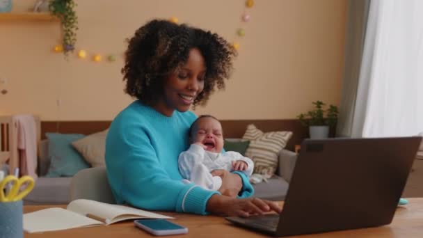 母性休暇中の若いアフリカ系アメリカ人のビジネスマンのミディアムショットは 家からラップトップに取り組み 彼女の泣いている小さな赤ちゃんの男の子を慰めます 戦闘おもちゃ — ストック動画