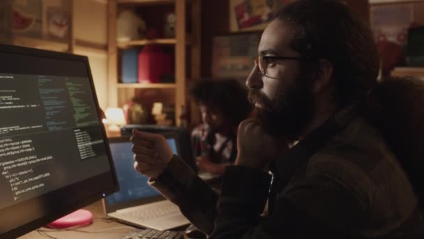 中东长发程序员在计算机显示屏上检查黑色背景下的程序代码时的翘起镜头 — 图库视频影像