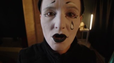 Yetişkin kadın pandomimci sanatçının sahne arkasında sahne arkası oyunculuğuna hazırlanırken yüzünü ekşitmesi ve kapıyı çalması.