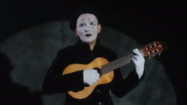 Gözyaşı makyajlı yetişkin pandomimci kadının karanlık sahnede sahne ışıkları altında ukulele çalarkenki görüntüsü.