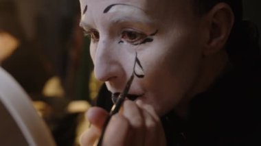Yetişkin pandomimci aktrisin üzgün makyajını yaparken yüzüne siyah gözyaşı sürerken sahne arkası gösterisine hazırlandığı orta ölçekli bir çekim.