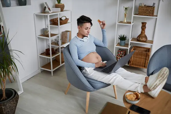 现代孕妇在家中休息和吃零食时使用笔记本电脑的全长肖像 — 图库照片