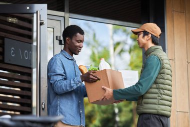 Siyahi bir gencin açık hava alışverişini kabul edip gülümsemesinin yan görüntüsü.