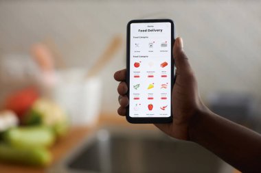 Tanımlanamayan siyahi adam elinde online alışveriş uygulaması olan akıllı telefon tutuyor. Kameraya bakkal uygulaması, kopyalama alanı
