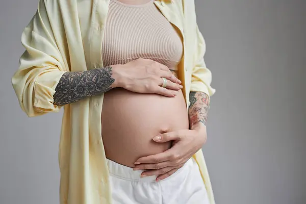 有纹身的怀孕年轻女子在工作室里抱着肚子 复制空间 — 图库照片