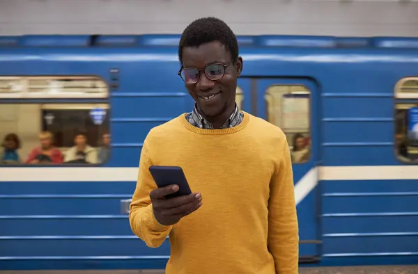 戴眼镜的商人一边站在地铁里一边看手机上的视频 一边带着背景微笑 — 图库照片