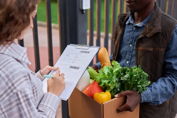 Closeup of young woman signing document accepting food delivery outdoors