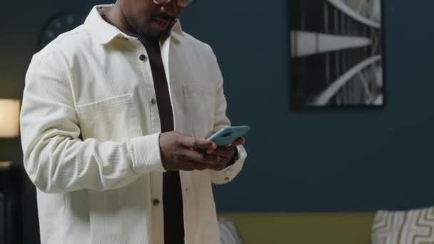 現代のミニマリストスタイルのオフィスの真ん中に立っている白いデニムジャケット ワイヤレスイヤホンを身に着けている現代黒人のミディアムショット — ストック動画
