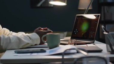 Bilgisayarda oyun oynayan genç siyahi bir adamın karanlık odada tek başına otururken yan görüş açısını yukarı kaldır.