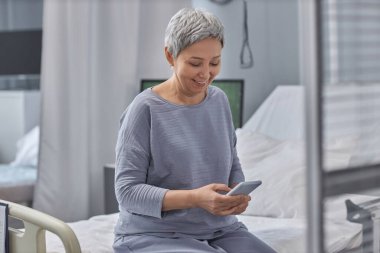 Üst düzey hasta cep telefonundan mesaj okuyor ve hastane koğuşunda yatarken gülümsüyor.
