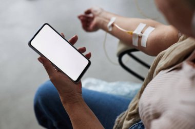 Serum tedavisi sırasında akıllı telefonu boş ekranla tutan yaşlı kadının yakın plan fotoğrafı.