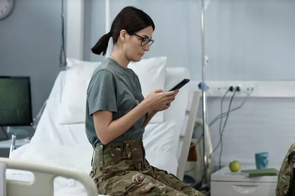 Unge Kvinnelige Soldat Skrive Melding Smarttelefon Mens Sitter Sengen Menigheten – stockfoto