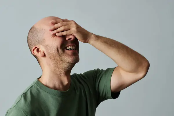 Candid portrait of mature bald man laughing emotionally with eyes closed against pale grey background