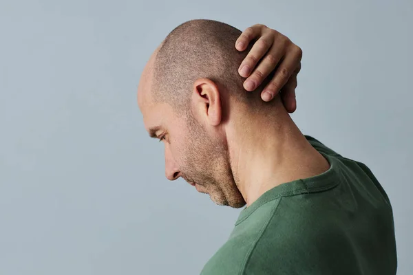 Minimal side view portrait of mature bald man touching head against pale grey background, copy space