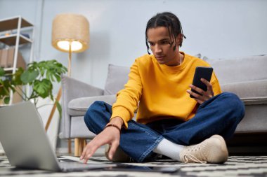 Evdeki yerde otururken dizüstü bilgisayar kullanan zenci bir gencin tam boy portresi, boşluğu kopyala