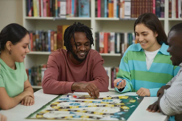 Diverse group of young people playing board games together in library and smiling