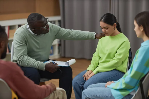 Portrait of black man as male psychologist comforting teenage girl in therapy session