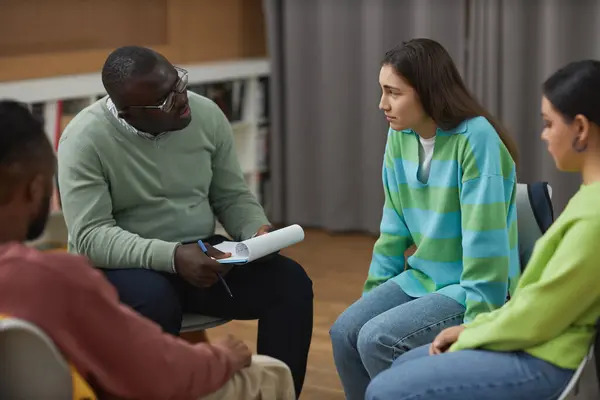 Portrait of black adult man as psychologist consulting group of teenagers in therapy session