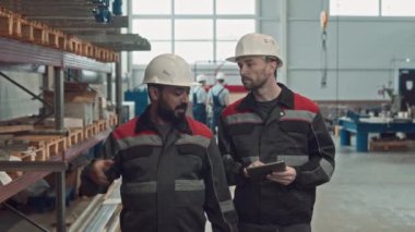 Orta Doğu ustabaşının genç beyaz iş arkadaşıyla birlikte sanayi fabrikasında teftiş yaparken dijital tabletle ilgili notlar alırken orta boy fotoğrafı.
