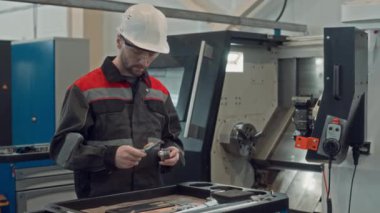 Beyaz tenli erkek bitki teknisyeninin iç mekanik ekipman onarımı yaparken donanım aletleri kullanarak tulum, şapka ve güvenlik gözlüğü taktığı orta boy bir fotoğraf.