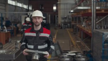 Kafkas erkek teknisyen iş kıyafetleri ve sert şapka taşıyarak ağır paslanmaz çelik ekipman taşıyarak endüstriyel fabrika boyunca, tamir ve montaj